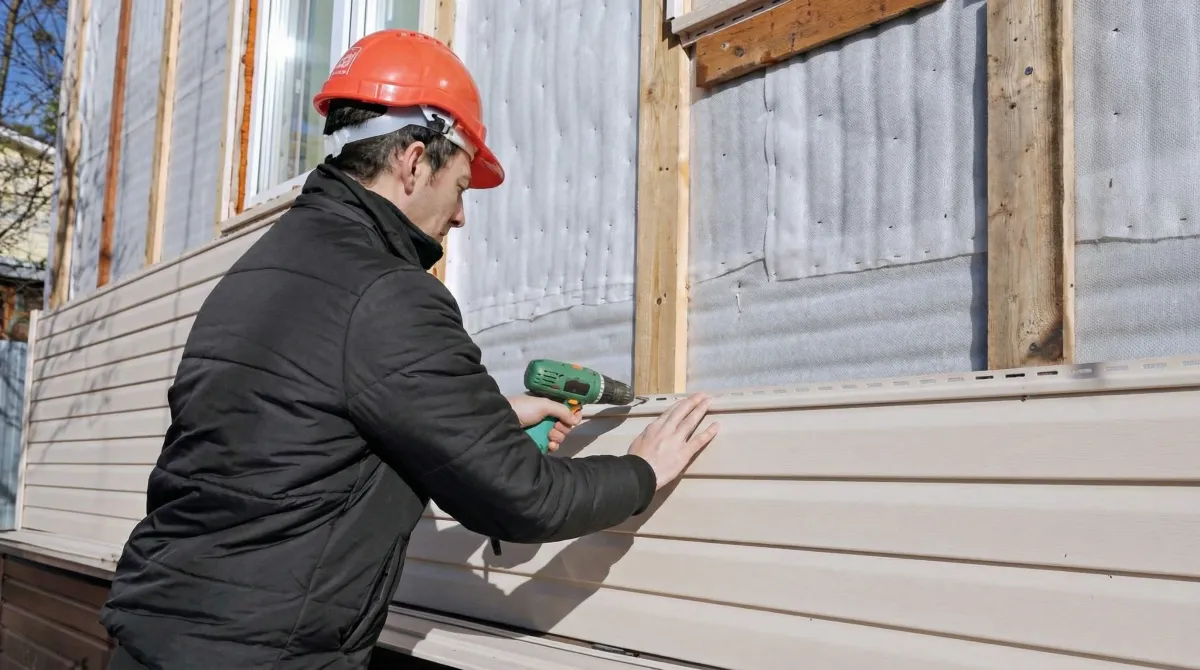 Siding replacement professional using a power drill to install new tan vinyl siding on a home exterior in Stamford, CT